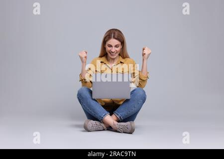 Emotionale Frau mit Notebook auf hellgrauem Hintergrund Stockfoto