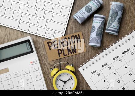 Karte mit Wörtern Pensionsplan, Banknoten, Taschenrechner und Wecker auf hölzernem Bürotisch, flach liegend Stockfoto