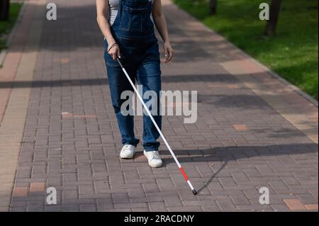 Eine gesichtslose blinde schwangere Frau läuft mit einem Stock die Straße entlang. Stockfoto