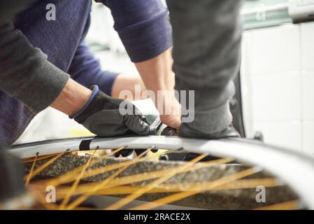 Zwei unbekannte Männer entfernen einen luftlosen Reifen von einem Rad in einer Fahrradwerkstatt. Selektive Fokuszusammensetzung mit Kopierbereich. Stockfoto