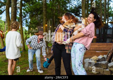 Lustiger Familienmoment mit dem Vater, der einen Gartenbläser benutzt, um seine Frau und seine Tochter zu ärgern, die Hunde halten Stockfoto