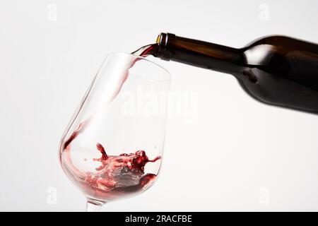 Rotwein, der aus der Flasche in ein geneigtes Weinglas gefüllt wird. Stockfoto