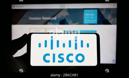 Person, die ein Mobiltelefon mit dem Logo des US-amerikanischen Kommunikationsunternehmens Cisco Systems Inc. Auf dem Bildschirm vor der Webseite hält. Konzentrieren Sie sich auf das Display des Telefons. Stockfoto
