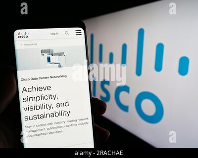 Person, die ein Mobiltelefon mit einer Webseite des US-amerikanischen Kommunikationsunternehmens Cisco Systems Inc. Auf dem Bildschirm mit Logo hält. Konzentrieren Sie sich auf die Mitte des Telefondisplays. Stockfoto