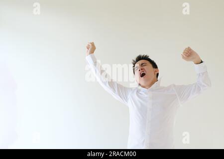 Ein junger asiatischer Mann, der ein weißes Hemd und eine Uhr trägt und seinen Körper dehnt. Isolierter weißer Hintergrund. Stockfoto