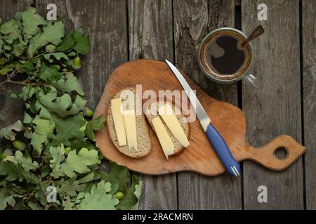 Zwei Sandwiches mit Käse auf einem Brett neben Kaffee und ein Eichenzweig auf dem Tisch in der Küche Stockfoto