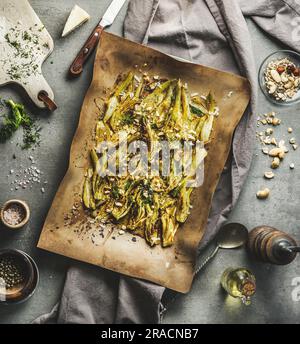 Gebratener Fenchel garniert mit Nüssen und Kräutern auf Backpapier auf dem Küchentisch mit Zutaten und altmodischen Utensilien. Draufsicht Stockfoto
