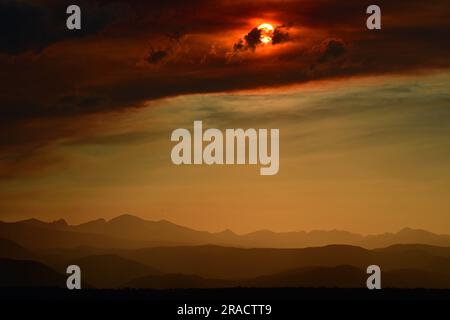 Farbenfroher Sonnenuntergang über der vorderen Ranch der felsigen Berge durch den rauchigen Dunst des Quellbachs, Wildfeuer in der Nähe des Fallschirms, aus der Sicht des Besen Stockfoto