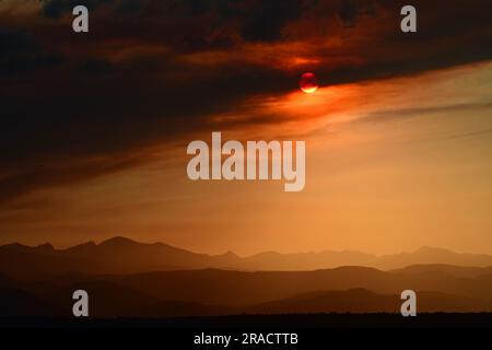 Farbenfroher Sonnenuntergang über der vorderen Ranch der felsigen Berge durch den rauchigen Dunst des Quellbachs, Wildfeuer in der Nähe des Fallschirms, aus der Sicht des Besen Stockfoto