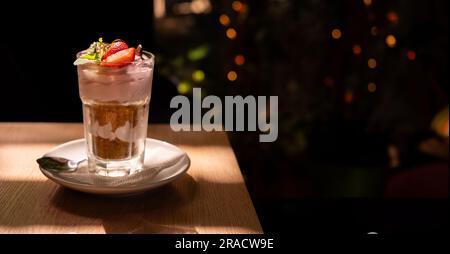 Italienisches Erdbeertiramisu mit Mascarpone, Savoyardi Crumb und frischen Erdbeeren in Glas im Café vor dunklem Hintergrund. Das Rezept der Einfachheit Stockfoto