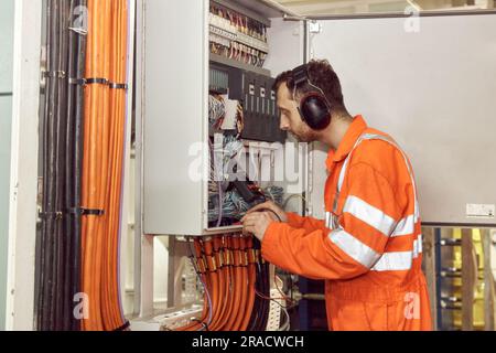 Offizier für Schiffselektrik prüft Schalttafel mit digitalem Multimeter. Junge Öl- und Gasexpertin. Stockfoto