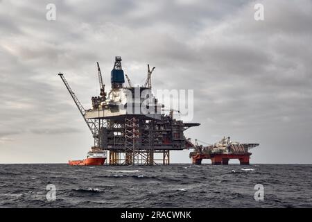 Offshore-Erdöl- und -Erdgasplattform mit Versorgungsschiff, das Frachtaktivitäten durchführt. Dunkler Himmel in der Nordsee. Stockfoto