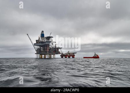 Bohren Sie die Bohrinsel, die halbtauchfähige Plattform und das Versorgungsschiff an einem dunklen bewölkten Tag im Meer auf. Stockfoto