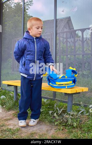 Der kleine Schuljunge wartet an der Bushaltestelle auf seinen Bus zur Schule Stockfoto