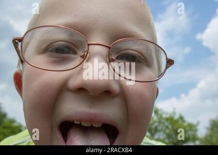 Ein lustiger kleiner Junge in der Brille zeigt eine Zunge Stockfoto