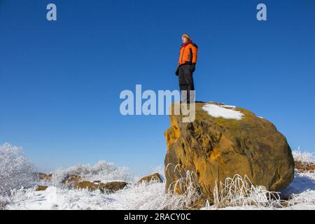 Auf einem großen Felsen steht ein junger Mann im Winter und sieht die Schönheit eines Wintermorgens Stockfoto