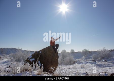 Der Typ sitzt auf einem Felsen und wird im Winter fotografiert Stockfoto