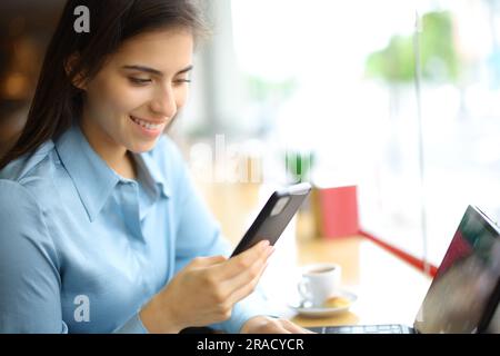 Glückliche Frau, die Handy und Tablet in einer Bar benutzt Stockfoto
