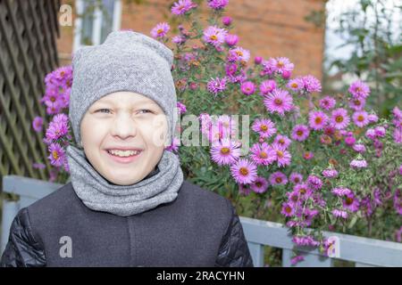 In einem grauen Mantel und Hut lächelte der Junge im Herbst Stockfoto