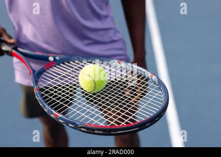 Mittelteil eines afroamerikanischen männlichen Tennisspielers, der Tennisschläger und Ball auf dem Freiluftplatz hält Stockfoto