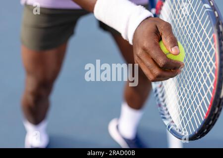 Mittelteil eines afroamerikanischen männlichen Tennisspielers, der Tennisschläger und Ball auf dem Freiluftplatz hält Stockfoto