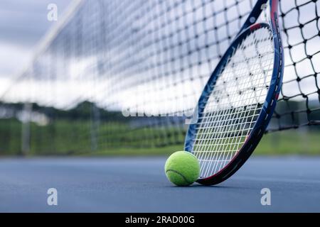 Nahaufnahme von Tennisball und Tennisschläger gegen Netz auf Tennisplatz an bewölktem Tag, Kopierbereich Stockfoto