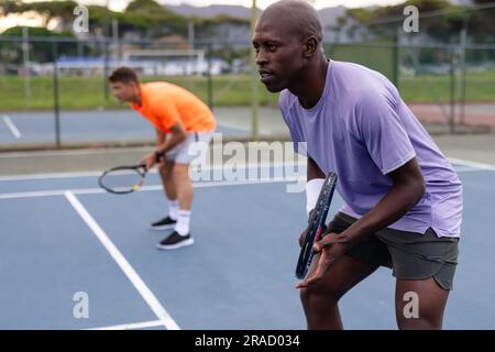 Fokussierte, vielfältige männliche Tennisspieler, die Doppel auf dem Outdoor-Platz spielen Stockfoto