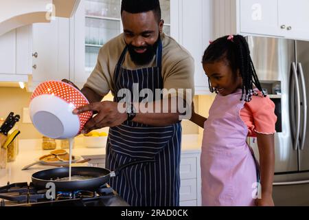 Glücklicher afroamerikanischer Vater mit Tochter, die Pfannkuchen in der Pfanne in der Küche kocht Stockfoto