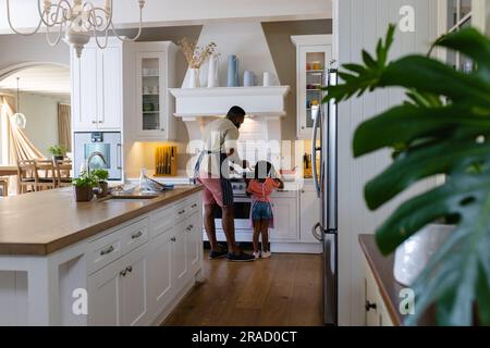 Rückansicht des afroamerikanischen Vaters und der afroamerikanischen Tochter beim Kochen von Pfannkuchen in der Küche Stockfoto