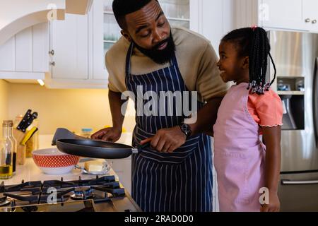 afroamerikanischer Vater mit lächelnder Tochter, die Pfannkuchen in der Pfanne in der Küche kocht Stockfoto