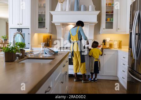Rückansicht einer afroamerikanischen Mutter mit Sohn, die Pfannkuchen in der Küche kocht Stockfoto