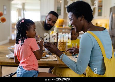 afroamerikanische Mutter fütterte die Tochter mit Pfannkuchen, während sie mit der Familie am Tisch frühstückte Stockfoto