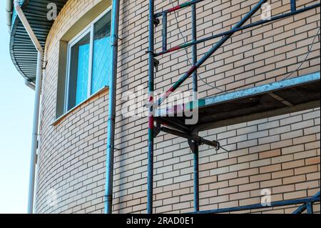 Backsteinwand und Gerüst. Gerüste in der Nähe des Gebäudes. Bau- und Renovierungsindustrie. Stockfoto