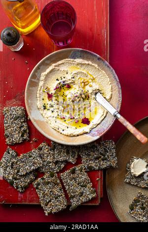 Hummus mit schwarzem Kreuzkümmel, Pinienkernen, essbaren Blumen und Samenknackern Stockfoto