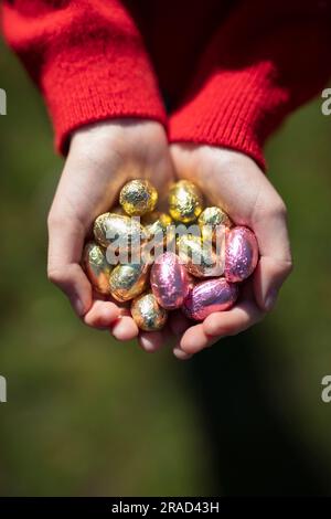 Kinderhände mit vielen kleinen, eingepackten Schokoladen-Ostereiern Stockfoto