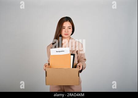 Traurige junge Geschäftsfrau, die eine Kiste voller Sachen hält, sich traurig fühlt, nachdem sie ihren Job gekündigt hat, weißer, isolierter Hintergrund. Stockfoto