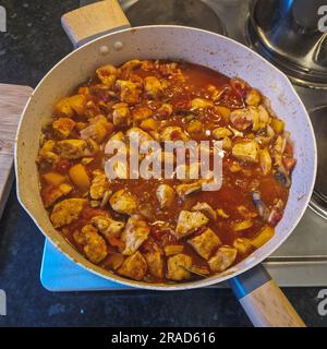 n Dieses fesselnde Bild erweckt die Kunst des Kochens zum Leben, wenn ein schmackhaftes Gulasch in einer Pfanne zubereitet wird. Die Szene ist in einer warmen und einladenden Küche Stockfoto