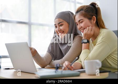 Eine fröhliche muslimische Frau und ihre Freundin sehen sich zusammen Filme in ihrer Freizeit an Stockfoto