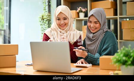 Eine glückliche junge asiatische muslimische Online-Verkäuferin, die mit ihrem Mitarbeiter im Büro arbeitet. KMU, Inhaber eines Online-Shops Stockfoto