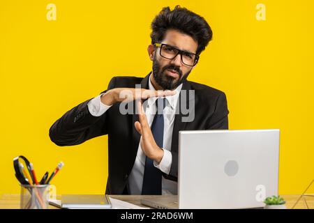 Ein müder, aufgebrachter indischer Geschäftsmann, der eine Auszeit-Geste, ein Limit- oder Stoppschild zeigt, kein Druck, ich brauche mehr Zeit am Arbeitsplatz im Büro. Hindu-Mann, der an einem Laptop arbeitet, isoliert auf gelbem Hintergrund Stockfoto