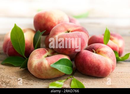 Frische Pfirsiche mit Blättern auf Holzgrund. Donut oder Weinberg Art von flachen Pfirsich. Stockfoto