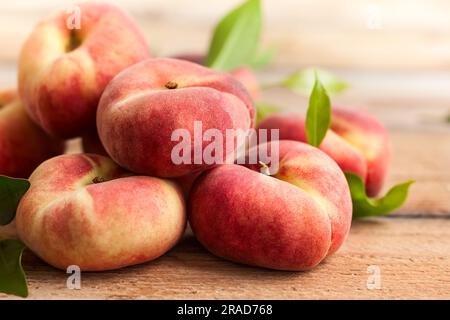 Frische Pfirsiche mit Blättern auf Holzgrund. Donut oder Weinberg Art von flachen Pfirsich. Stockfoto