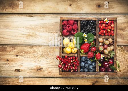 Mix aus frischen Beeren mit Blättern in Vintage-Holzkiste auf rustikalem Holzhintergrund. Draufsicht. Rohe, gesunde Lebensmittel. Verschiedene Beeren. Stockfoto