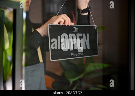 Der junge asiatische Coffee Shop-Besitzer eröffnet seinen Laden und dreht das Schild für das Café auf. schild, Symbol, verfügbar Stockfoto