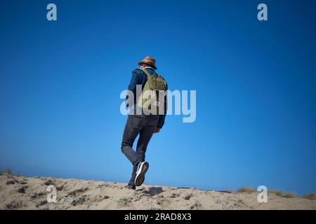 Ein Mann mit blauen Jeans und Strohhut genießt einen Spaziergang in den Dünen Stockfoto