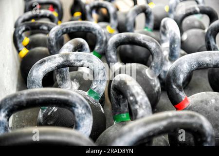 Nahaufnahme einer Reihe von schweren Metallkettlebells mit bunten Streifen und Griffen, die auf dem Boden in einem modernen, leichten Fitnessstudio gestapelt sind Stockfoto