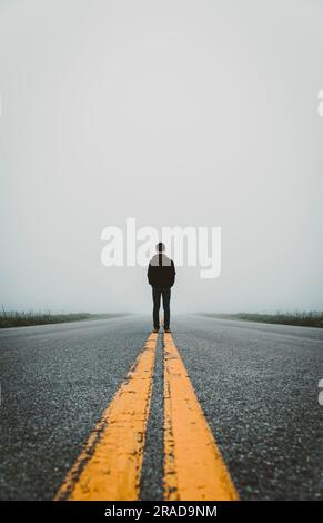 Ein Teenager, der an einem nebligen Tag mitten auf der Landstraße steht. Stockfoto