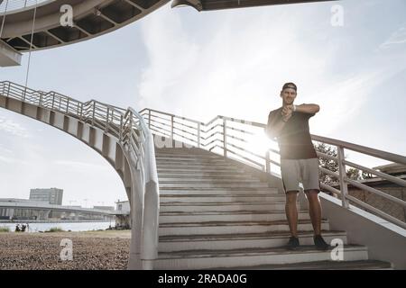 Ein junger Sportler steht auf der Treppe und schaut nach einem netten Joggen auf seine Smartwatch. Stockfoto