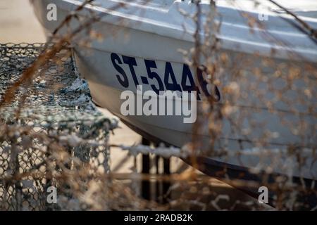 Das Fischerboot blickt durch alte Fischernetze an einem Kai neben einem Haufen Krabben und Hummertöpfen. Stockfoto