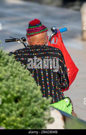 Ein alter, gebräunter Mann, der auf einer Bank in einem Studiengang saß, kroatien, ein älterer Mann, der farbenfrohe Mütze und Kleidung trug, mit einem Fahrrad, das sich auf dem Heimweg entspannte. Stockfoto